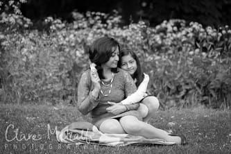 Black and white photograph of mother and daughter sitting on grass with flowers behind. 