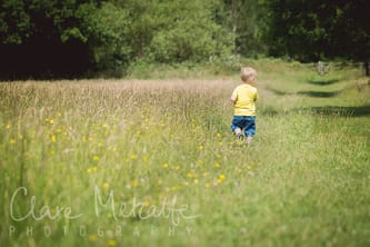Photograph of child walking away in field of buttercups.