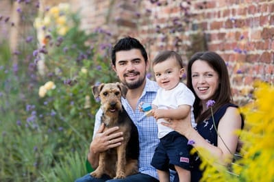 Photograph of family with baby and dog sitting in a walled garden. 