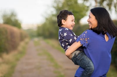 Photograph of mother and son smiling at each other outside in country lane. 