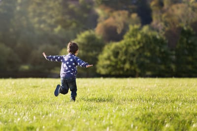 Photograph of a boy pretending to be an airplane in a field.