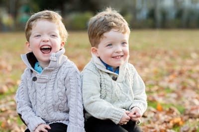 Photograph of twin boys laughing in autumnal scene.