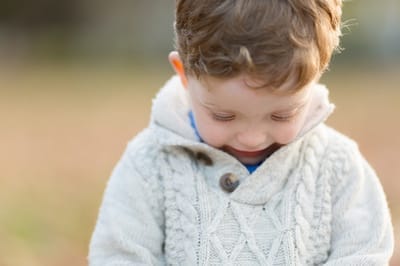 Photograph of little boy in ribbed jumper looking down. 